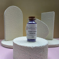A small glass vial of paint pigment powder by Healing Hearts & Crafts in Imperial Earth sits on a textured white cylindrical pedestal. The vial contains deep purple pigment powder and has a cork stopper.