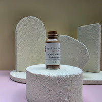 A small glass bottle of Healing Hearts & Crafts Pigment Powder in Smoked Walnut stands on a round textured pedestal, with matching textured display blocks behind it against a beige background.